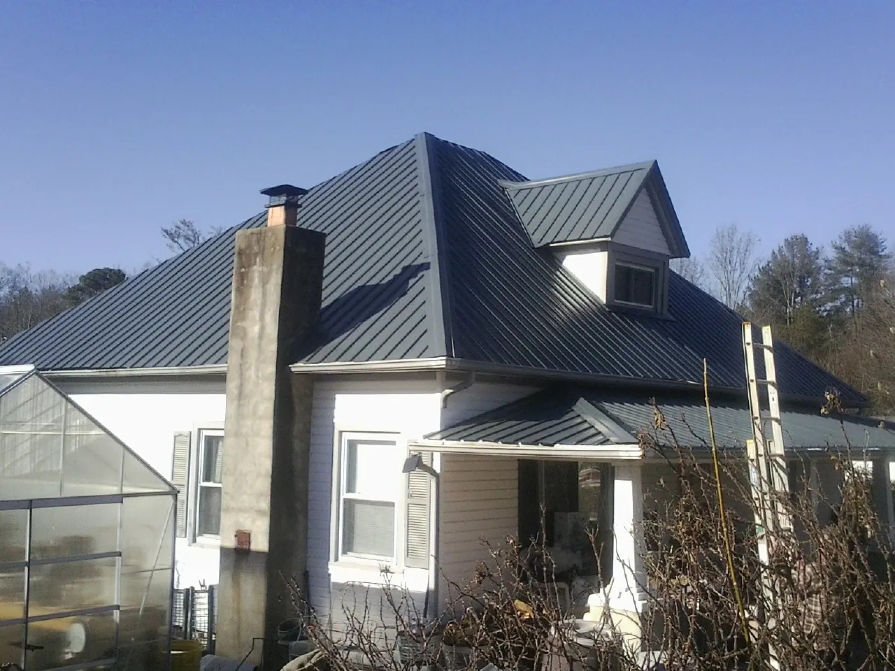 Dark blue standing seam metal roof on a white farmhouse with dormer — Slate & Tile Roof Repair by Roofing Brothers in East Springfield