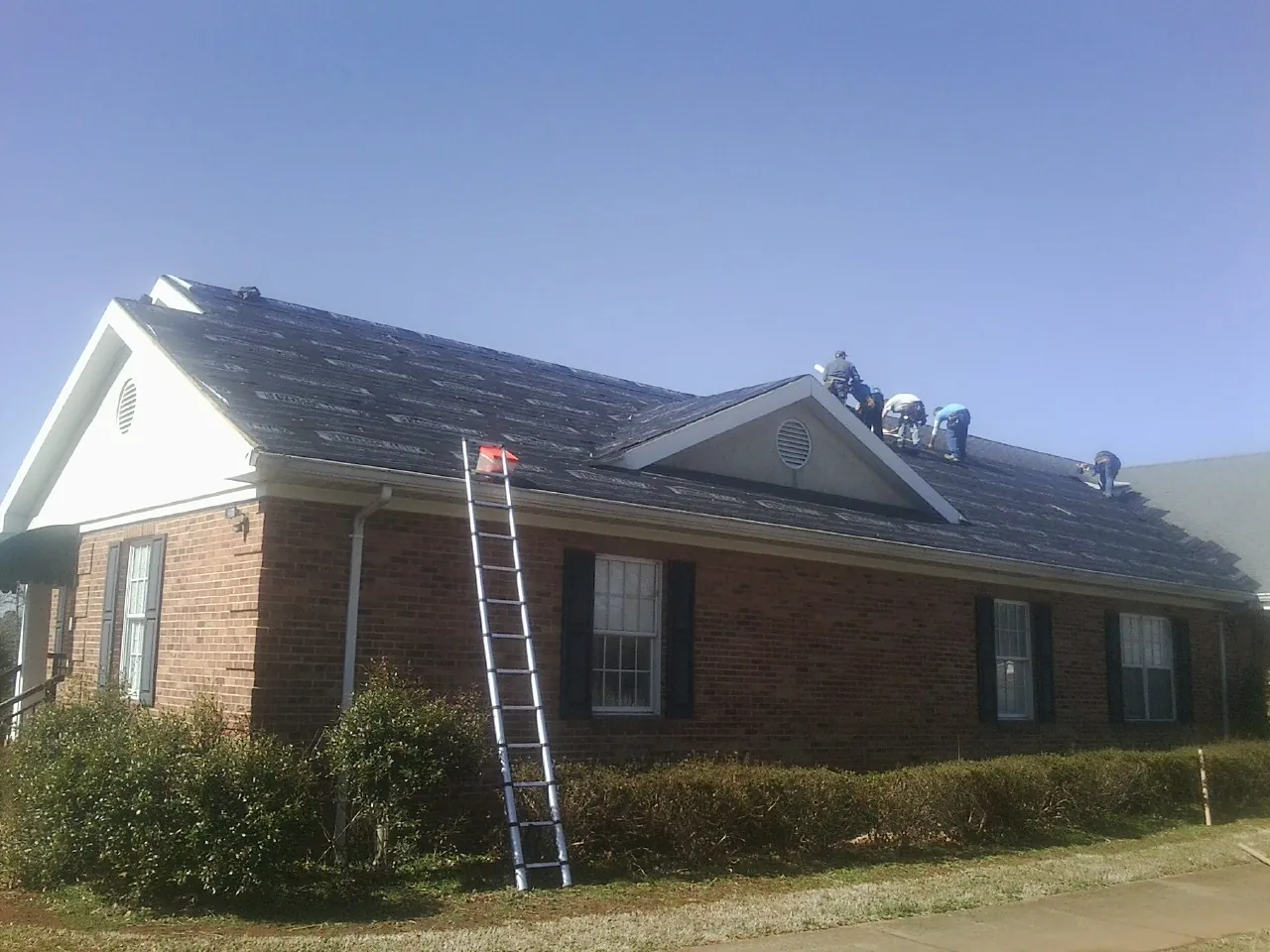 Crew tearing shingles off a brick ranch roof with a ladder set — Metal Roof Repair work by our crew in East Springfield