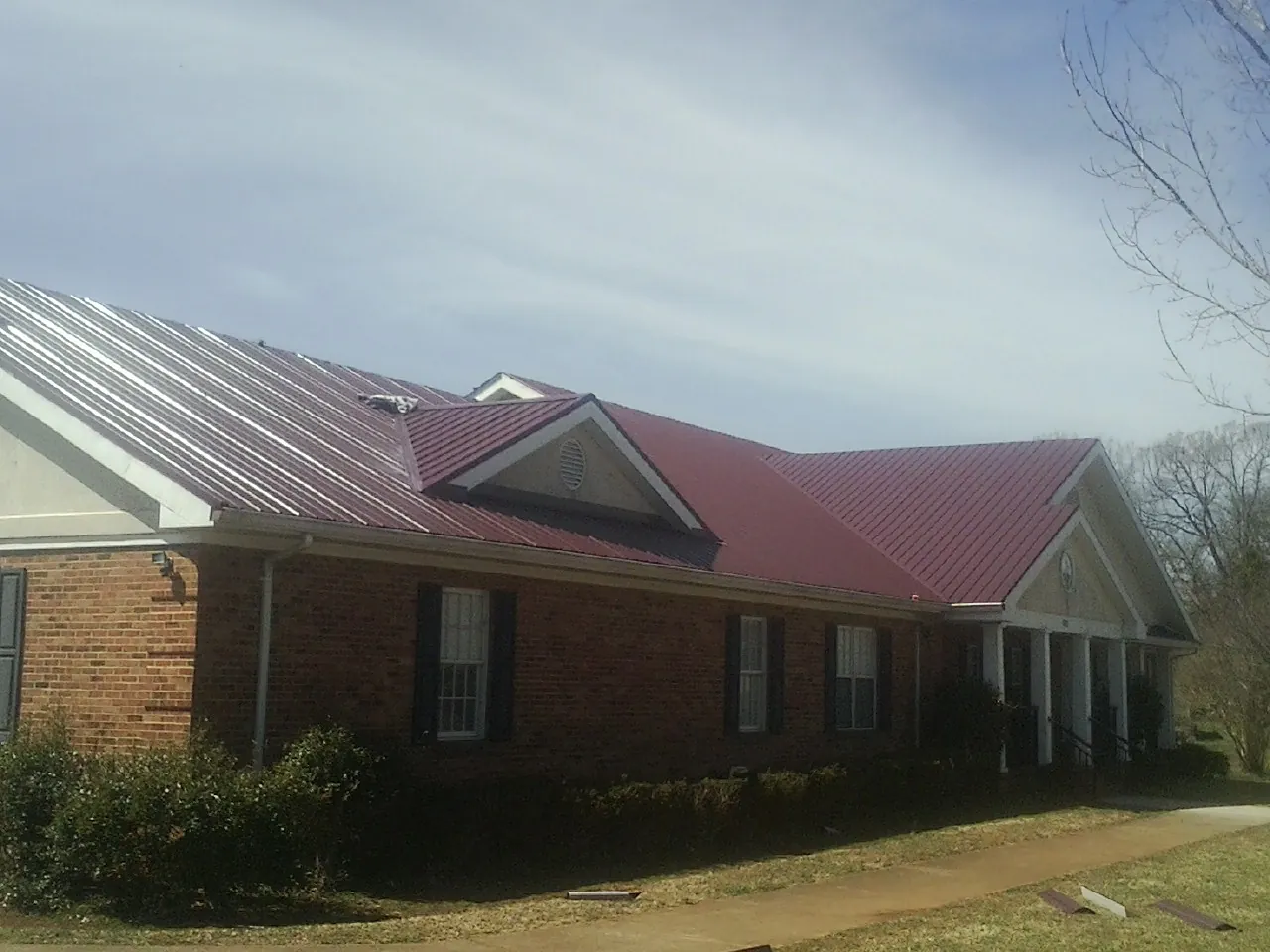 Red metal roof with gabled entries on a long brick building, from a Hail Damage Roof Repair job in East Springfield