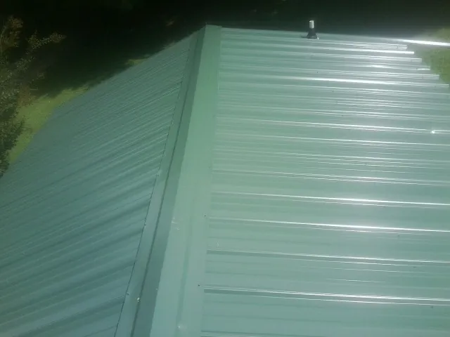 New green metal panels meeting at the ridge of a roof — Flat Roof Repair work by our crew in East Springfield